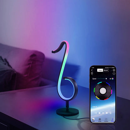 Music note-shaped lamp with RGB lighting and smartphone app control on a bedside table.